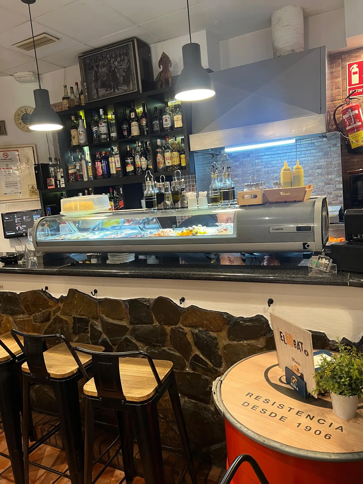 La barra de la Tapería El Beato: vitrina de tapas, botellas y taburetes